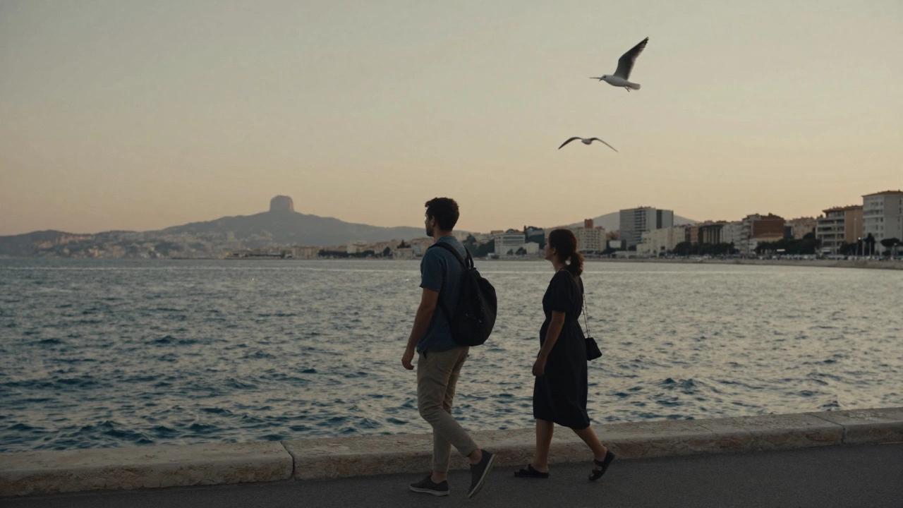 Two individuals walking calmly along the Corniche in Marseille at dusk, sea and cliffs visible behind them.